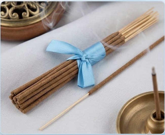 Bundle of sandalwood incense sticks tied with a blue ribbon beside a brass holder